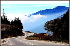 an image of a mountain road going through the foggy hills and clouds in the distance