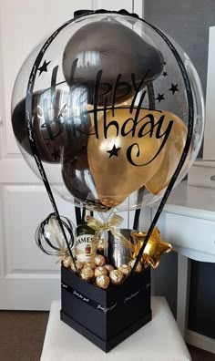 a bunch of balloons and chocolates in a black box on a white stool with the words happy birthday written on it