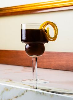 a close up of a drink in a wine glass on a marble counter top with a wooden frame behind it