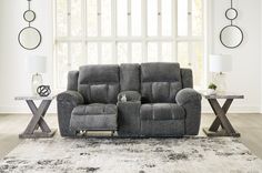 a gray reclining sofa sitting on top of a rug in a living room next to a window