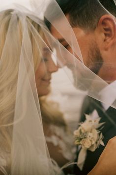 the bride and groom are looking at each other with veils over their heads in front of them