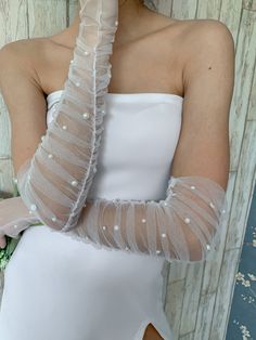 a woman in a white dress holding flowers and wearing long gloves with pearls on them