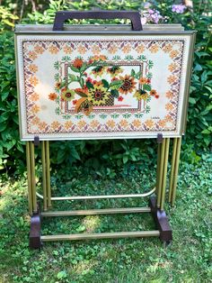 an old metal frame with flowers painted on it and some plants in the back ground