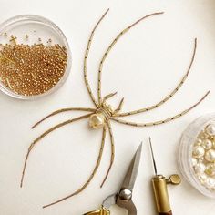 a spider made out of gold beads and scissors on a table with other crafting supplies