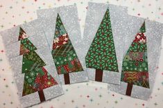 four small christmas trees are sitting on a white tablecloth with snowflakes and stars