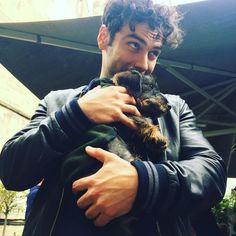 a man holding a small dog in his right hand and looking at the camera while wearing a leather jacket