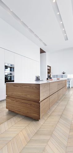 a kitchen with white walls and wood flooring on the side, along with an island