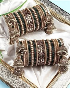 two sets of bangles are sitting on a tray with white cloth and green ribbon