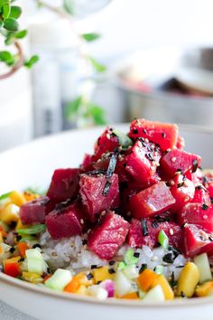 a white bowl filled with rice, watermelon and other vegetables next to a potted plant