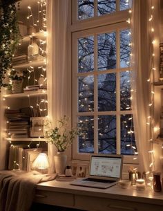 a laptop computer sitting on top of a desk next to a window covered in fairy lights