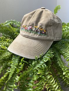 a tan hat with embroidered flowers on it sitting in the middle of some green plants