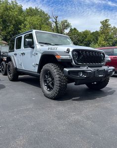 a white jeep parked in a parking lot next to other cars and trees on a sunny day