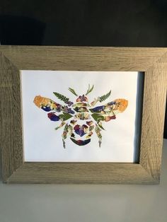 an art work with flowers and leaves in a wooden frame on a table next to a black wall