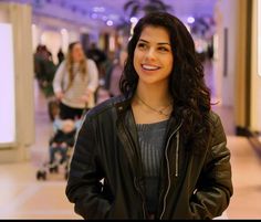 a woman standing in a mall with her hands on her hips and smiling at the camera