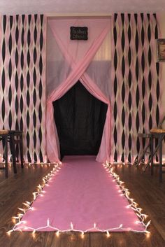 a pink carpet with lights on it in front of some curtains and chairs at the end