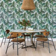 a dining room table with chairs and a plant on the wall next to it in front of a palm print wallpaper