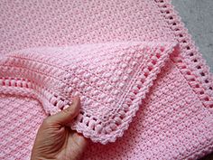 someone is holding up a pink crocheted blanket