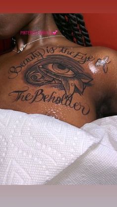 a woman laying in bed with tattoos on her chest and the words behind her back