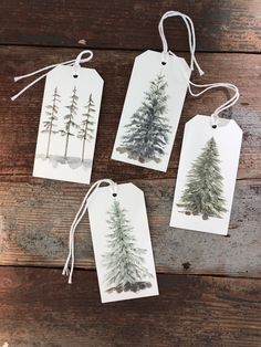 three tags with watercolor trees on them hanging from twine strings against a wooden background