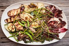 a white plate topped with vegetables and meat on top of a wooden table next to a fork