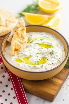 a bowl of dip with pita bread and lemons in the background on a cutting board