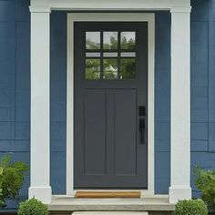 a gray front door on a blue house with white trim and columns, flanked by two potted plants