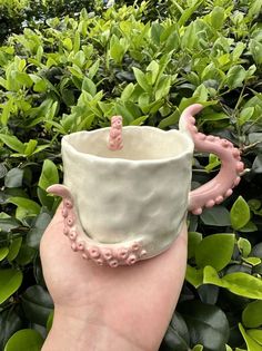 a hand holding a coffee cup with an octopus decoration on the outside and inside, in front of some bushes