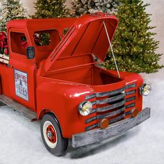 an old fashioned red truck with a christmas tree in the back and snow on the ground