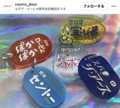 four different colored dog tags on a holographic background with japanese characters and words