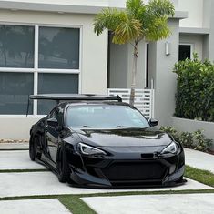 a black sports car is parked in front of a house with palm trees and grass