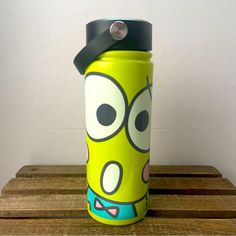 a green water bottle with a cartoon character on the front and black lid sitting on a wooden table