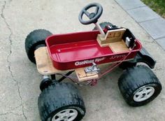 a red toy car with wheels and a steering wheel attached to the front, sitting on concrete