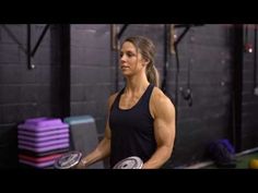 a woman holding two dumbs in a gym