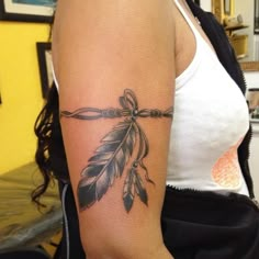 a woman's arm with a feather and arrow tattoo on the left side of her arm