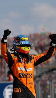 a man in an orange and black outfit holding his hands up while standing on top of a race track