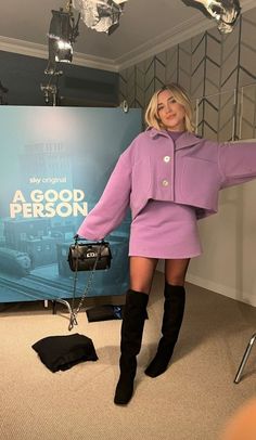 a woman in a purple coat and black boots posing for the camera with her hand on her hip