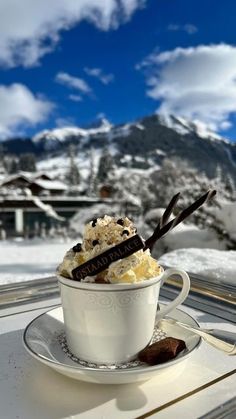 a cup filled with ice cream sitting on top of a saucer next to a snow covered mountain