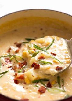 a close up of a spoon in a bowl of soup with cheese and bacon on top