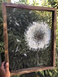 a person holding up a frame with a painting of a dandelion