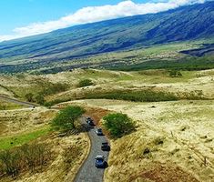 an aerial view of cars driving down a dirt road in the middle of a mountain range