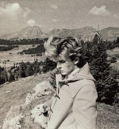 a black and white photo of a woman standing on top of a hill with mountains in the background