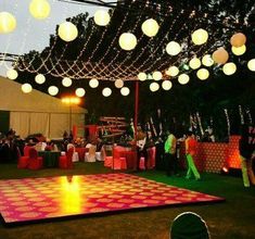 people are dancing on the dance floor at an outdoor event with paper lanterns hanging from the ceiling