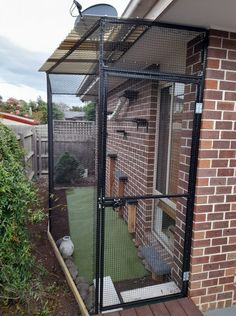 a black cage is on the side of a brick building with a green yard in front of it