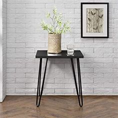 a small table with some plants on it in front of a white brick wall and wooden floor