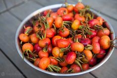 a metal bowl filled with lots of red berries on top of a wooden table next to water