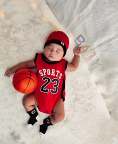 a baby is laying on the floor with a basketball in it's hand and wearing a red sports jersey