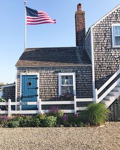 a small house with a flag on top of it and flowers in the front yard