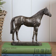 a horse statue sitting on top of three books next to a basket and potted plant