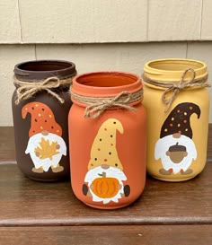 three painted mason jars sitting on top of a wooden table