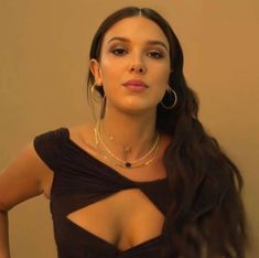 a woman with long hair wearing large hoop earrings and a black top is posing for the camera